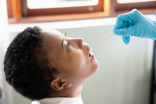 Afrikkalainen nainen, jolle tehdään kurkkutesti; käsite yleinen COVID-19-testaus, kontaktien jäljitys, valtion karanteeni, terveydenhuollon työntekijän riski, koronaviruksen havaitseminen sylkinäytteestä PCR-menetelmällä - Valokuva, kuva