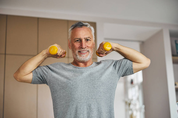 Energetic aged gentleman lifting dumb-bells and feeling good - Photo, Image