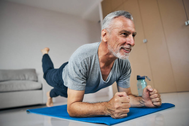 Здоровый пожилой человек тренирует мышцы выносливость в положении доски - Фото, изображение