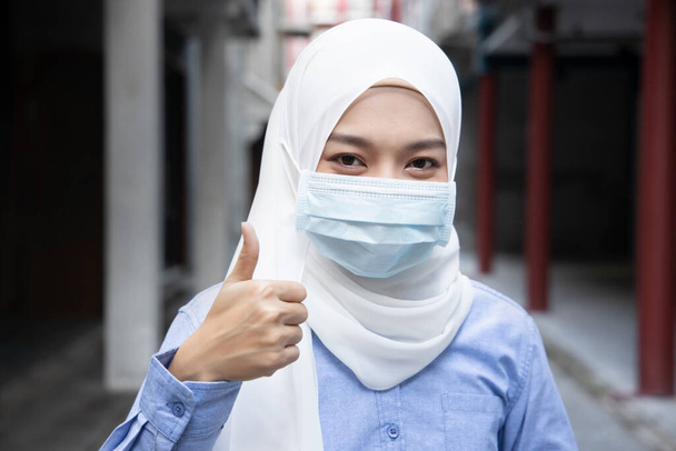 Donna musulmana che suggerisce di indossare maschera in pubblico all'aperto con pollice in su gesto; concetto di nuovo stile di vita normale, distanza sociale, appiattire la curva, misura preventiva contro l'influenza pandemica - Foto, immagini