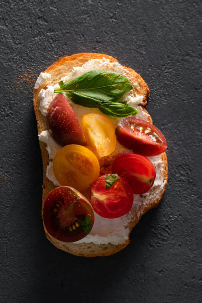 Bruschetta with curd cheese, cherry tomatoes and basil on a dark concrete background. Italian cuisine, breakfast sandwich. - Photo, image