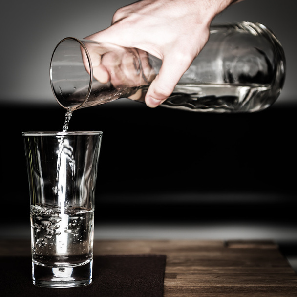 Hand fills in water with glass jug on wooden table - Photo, Image