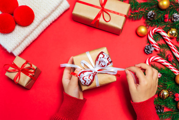 Prezenty świąteczne, dłonie dzieci otworzyć prezent noworoczny na czerwonym tle, Christmas kompozycja gałązki jodły z prezentów, złote dekoracje, czerwone kulki i karmel na czerwonej powierzchni - Zdjęcie, obraz