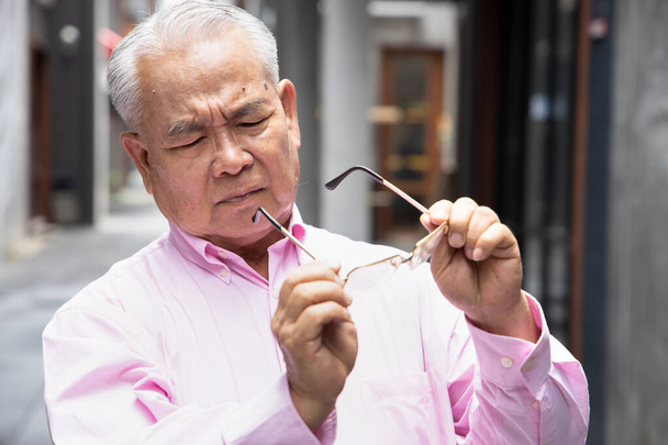 Asiatischer alter Mann leidet an Presbyopie, langer Sehfähigkeit oder Sehverlust mit verschwommenem Sehvermögen - Foto, Bild