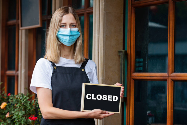 Caucasian waitress woman wearing medical mask holds SORRY WERE CLOSED. Coronavirus pandemic. Government shutdown of restaurants, shopping stores, non essential services - Foto, imagen