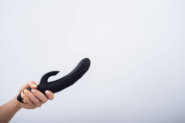 Faceless woman holding black dildo with clitoris stimulator on white background - Fotografie, Obrázek