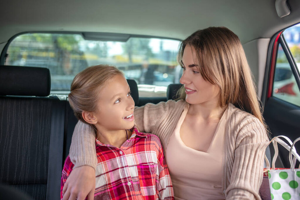 Happy mom hugging her daughter on backseat of car - Foto, Imagen