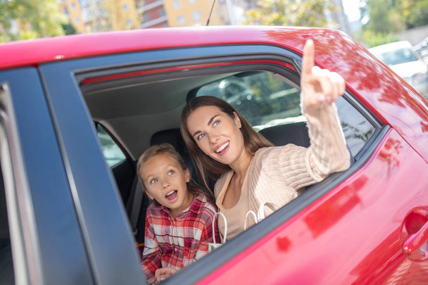 Girl looking out the window on backseat of car with her mom pointing upwards - Foto, imagen