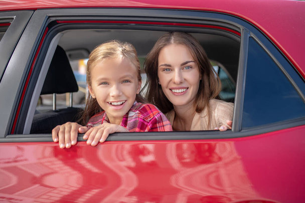 Happy daughter and her mom looking out the window on backseat of car - Photo, image