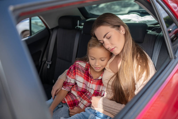 Pleased daughter and her mom hugging, napping on backseat of car - Fotó, kép