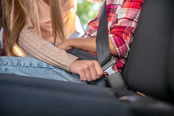 Close-up of female hands fastening girls safety belt on backseat of car - Fotografie, Obrázek