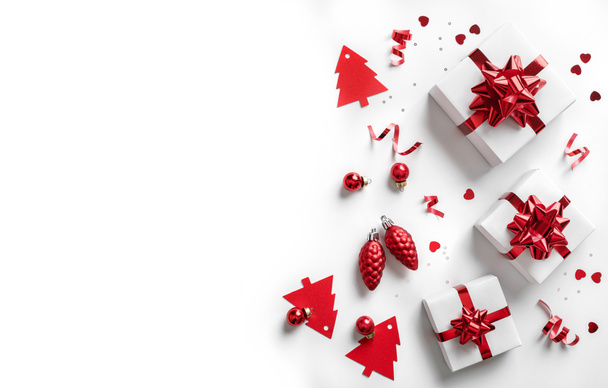 白い背景に赤い弓、装飾、輝きやコンフェッティとクリスマスギフトボックスで作られたメリークリスマスカード。Xmasとボケ、光、輝きと新年の休日のバナー。フラットレイアウト、トップビュー - 写真・画像