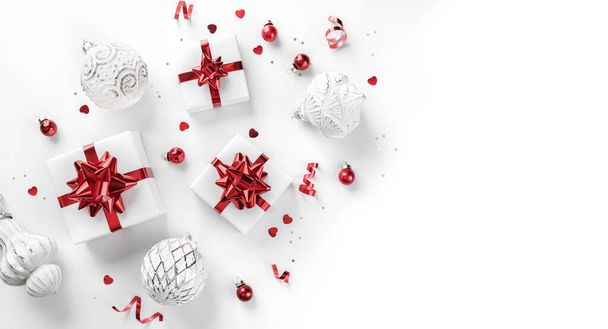 赤い弓、銀の装飾、輝きと白い背景にコンフェッティとクリスマスギフトボックスで作られたメリークリスマスカード。Xmasとボケ、光、輝きと新年の休日のバナー。フラットレイアウト、トップビュー - 写真・画像