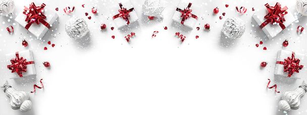 Весёлая рождественская открытка из рождественских подарочных коробок с красными луками, серебряными украшениями, блестками и конфетти на белом фоне. Рождественское и новогоднее праздничное знамя с боке, светом, блестками, видом сверху - Фото, изображение