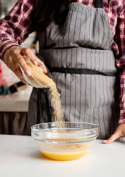 Junge lateinische Frau gießt Zucker in den Teig, der in der Küche kocht - Foto, Bild
