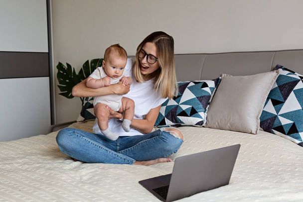 Telecommuting in quarantine. Mother showing baby to friends at the video chat. Stylish young freelancer working from home. Social distancing during coronavirus covid-19 pandemic concept. - Fotoğraf, Görsel