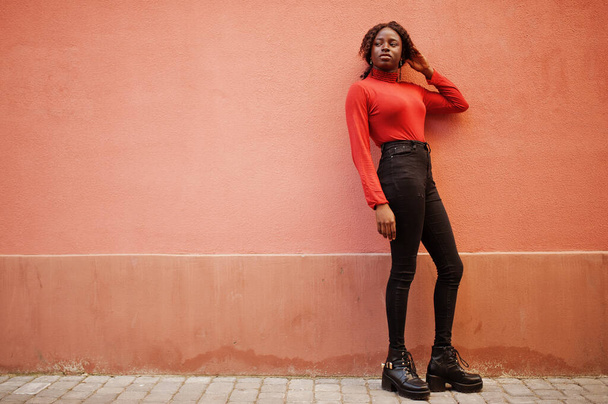 Portrait of a curly haired african woman wearing fashionable red turtleneck posing against rose wall. - Foto, Bild