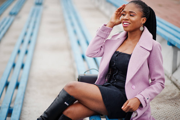 Young stylish beautiful african american woman in street at the stadium bleachers, wearing fashion outfit coat. - Photo, Image