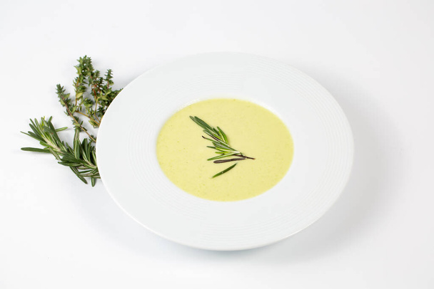 Ein Schuss Suppenteller mit Zucchini-Rahmsuppe auf einem weißen Tisch mit grünen Pflanzen - Foto, Bild