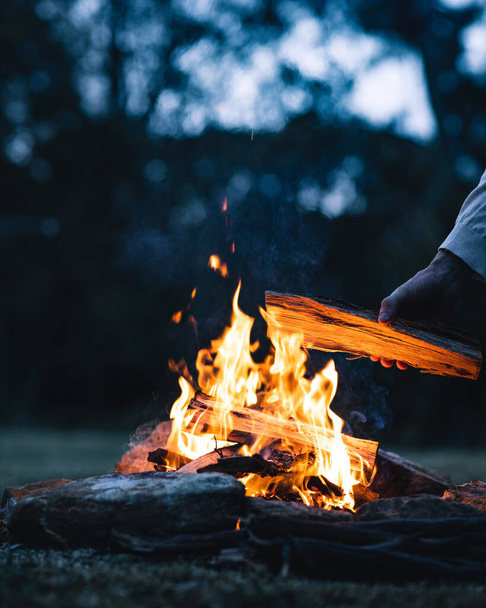 A man putting a log in a bonfire in the evening - Foto, Imagem