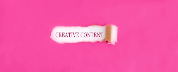 The text CREATIVE CONTENT appearing behind torn pink paper. - Photo, Image