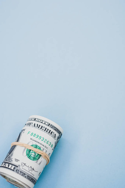 A vertical shot of a bundle of rolled-up American banknotes on a light blue background - Foto, afbeelding