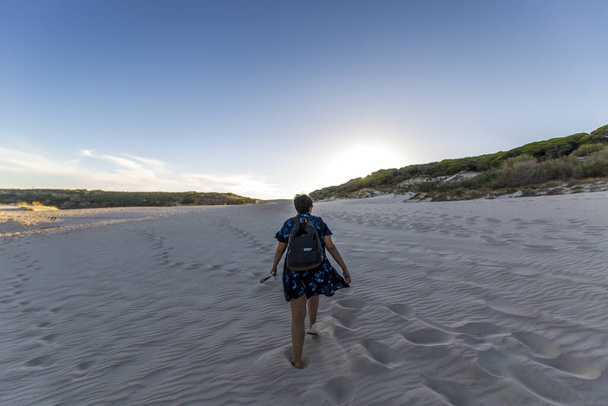 Vue de dos d'une jeune femelle marchant sur du sable blanc au coucher du soleil - Photo, image