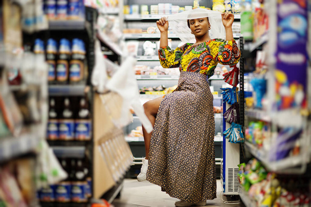 Happy african woman in traditional clothes and veil looking product at grocery store, shopping in supermarket.  Afro black  women costumer buying food at the market. - Foto, afbeelding