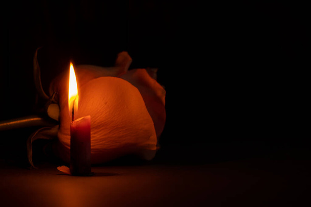 ένα κερί φλόγα και δίπλα σε ένα αυξήθηκε στο σκοτάδι close-up - Φωτογραφία, εικόνα