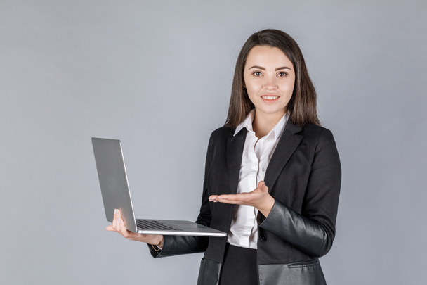 Young business woman in dark suite with laptop on grey background. Office concept - Foto, Imagem