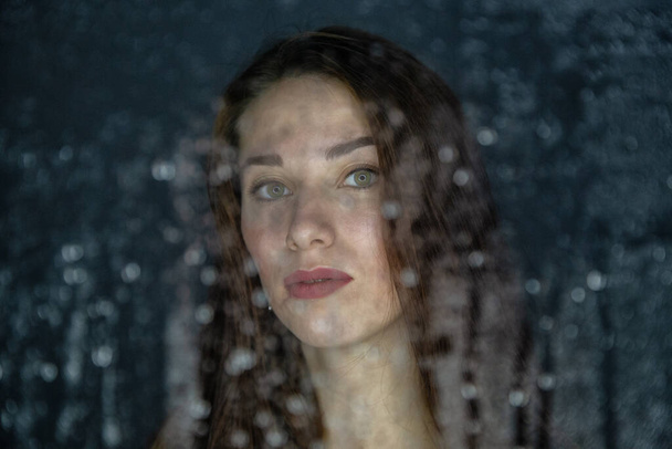 Portrait de jeune femme derrière un verre avec des gouttes d'eau - Photo, image