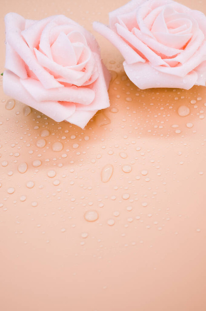 Un gros plan des roses décoratives artificielles sur la surface orange avec des gouttelettes d'eau - Photo, image