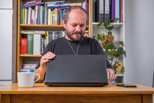 Мужчина работает онлайн из дома, с наушниками, закрывая ноутбук компьютера после онлайн видео встречи - Фото, изображение