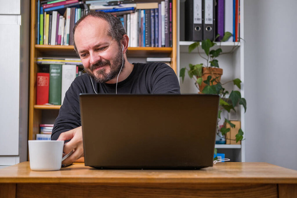 Człowiek pracujący online z biura domowego na laptopie komputerowym za biurkiem vintage, ze słuchawkami, słuchając spotkań online i pijąc kawę - Zdjęcie, obraz