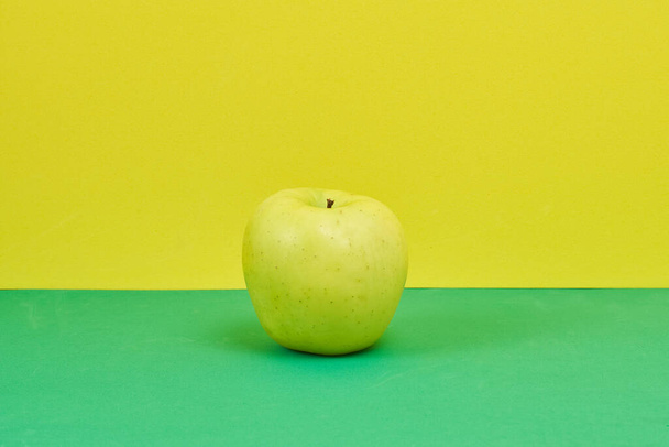A closeup shot of an apple on a green and yellow background - Foto, Imagen
