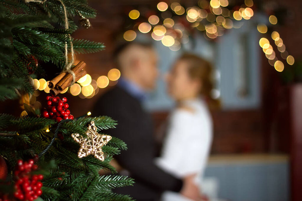 Διακοσμημένο χριστουγεννιάτικο δέντρο στο φόντο του αγκαλιάζει τον άνδρα και τη γυναίκα σε bokeh. Χριστουγεννιάτικο φόντο, ευχετήρια κάρτα σε ζεστά χρώματα - Φωτογραφία, εικόνα