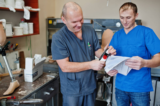 Deux prothésistes hommes travailleurs faisant la jambe prothétique tout en travaillant en laboratoire. - Photo, image