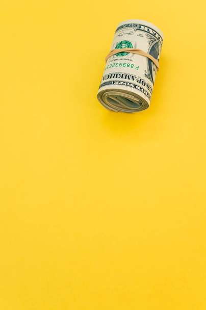 A vertical shot of rolled-up dollar bills on a yellow surface - Foto, afbeelding