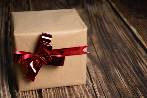 A closeup of a gift box with a red ribbon on wooden background - Zdjęcie, obraz