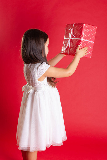 a girl in a white dress stands sideways and holds a red gift box, isolated on a vibrance background - Fotografie, Obrázek