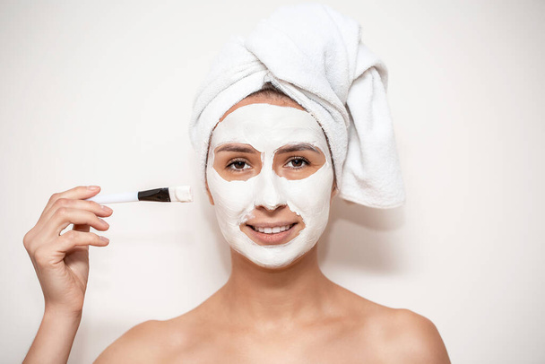 young woman with cosmetic mask on her face for detoxifying the skin and for black heads and acne on a white background. Skin care and spa treatments. - Photo, image