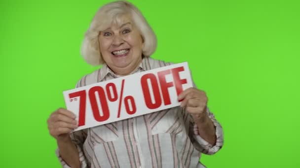 Senior grandmother showing Up To 70 percent Off inscription sign, rejoicing discounts. Chroma key - Footage, Video
