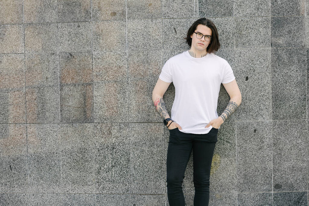 Hipster handsome male model with glasses wearing white blank t-shirt and black jeans with space for your logo or design in casual urban style - Foto, Imagem