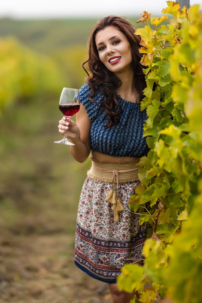 Eine schöne Frau mit einem Glas Rotwein im Weinberg an einem Herbsttag. - Foto, Bild