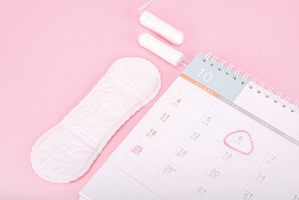 A period calendar, sanitary pads and tampons on a pink background - Foto, Imagen