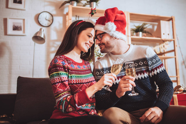 Bella giovane coppia sta tenendo bicchieri di champagne e sorridente mentre celebra a casa - Foto, immagini