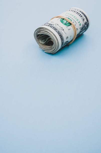 A vertical shot of a bundle of rolled-up American banknotes on a light blue background - 写真・画像