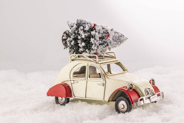 A closeup of a small vintage toy car with a Christmas tree on its roof on an artificial snow - Fotoğraf, Görsel