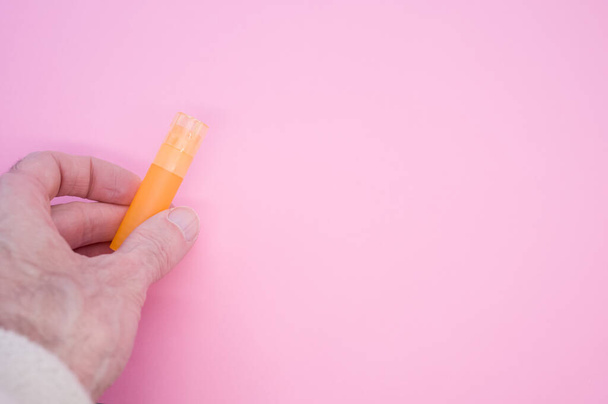 A hand holding an orange empty small plastic tube on pink background with a copy space - Foto, afbeelding