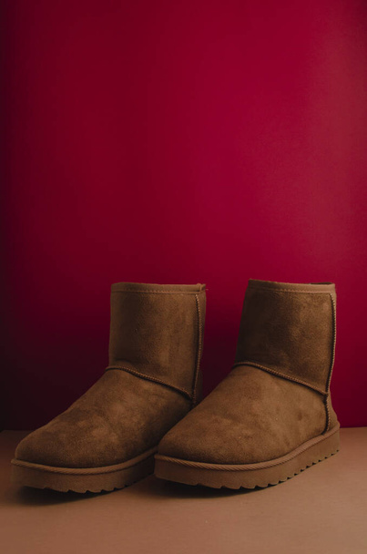 A vertical shot of a pair of brown winter ugg boots on a red background - Photo, Image
